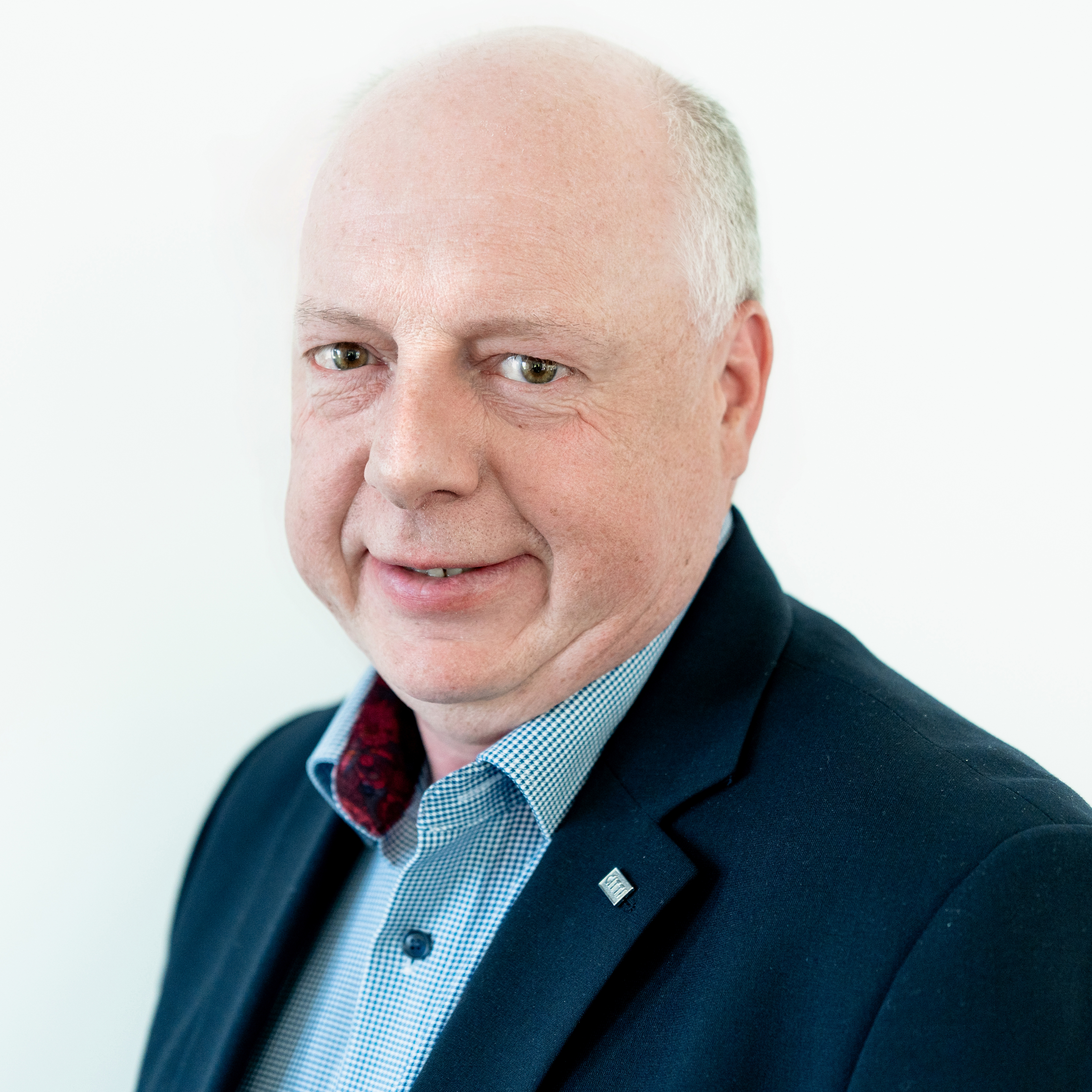 Mann mit grauen Haaren trägt einen Anzug und lächelt in die Kamera